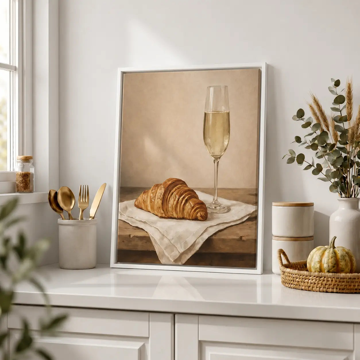 Framed artwork of a croissant and champagne glass on a kitchen counter with decor items.