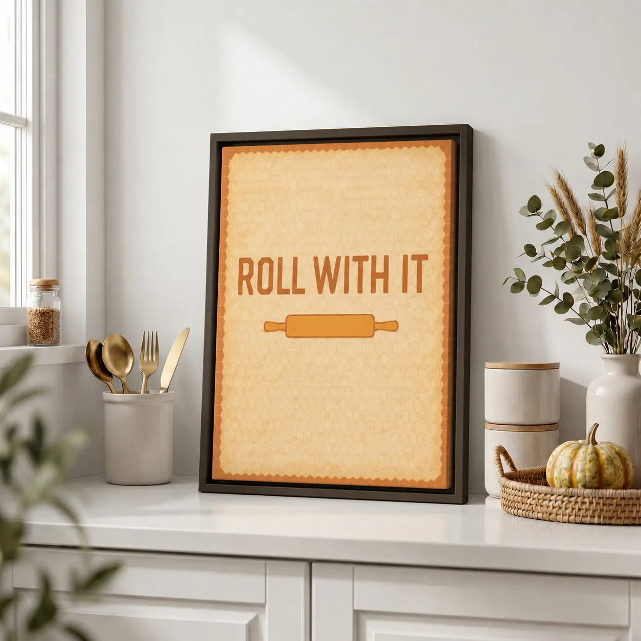Framed kitchen wall art canvas with 'Roll with It' text and rolling pin graphic on a kitchen counter.