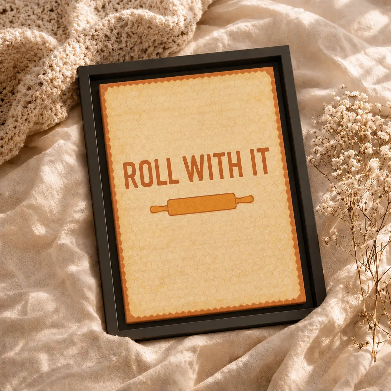 Framed motivational kitchen wall art canvas with 'Roll with It' text and rolling pin graphic on a textured fabric background.